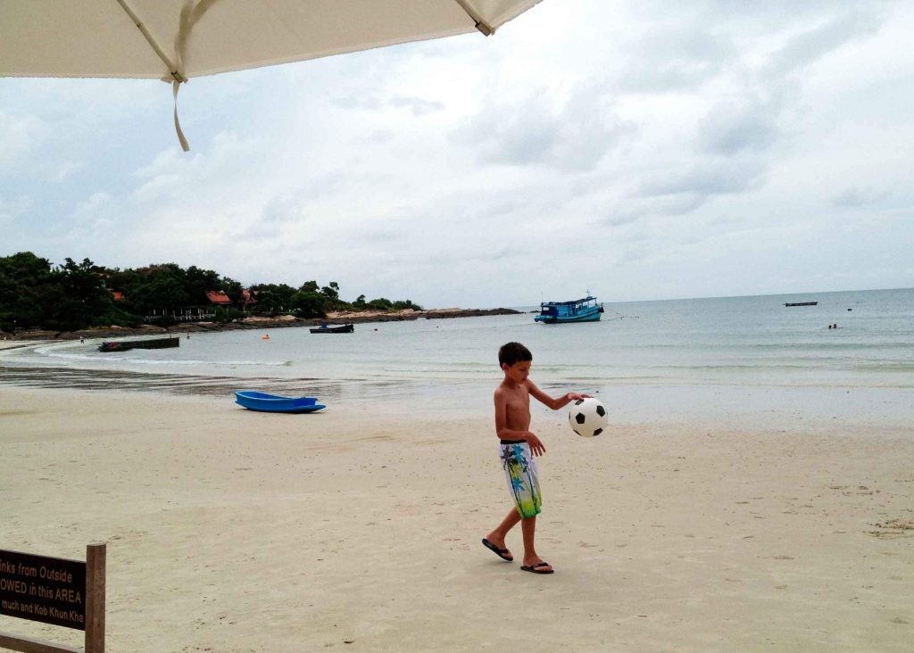 A boy playing with a ball on the beach in Koh Samet Thailand, wearing flip flops and a pair of swimming pants.