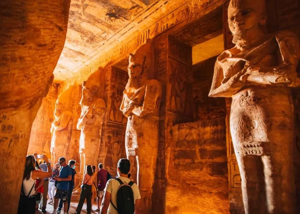 Inside the temple of Abu Simbel in Egypt, where lots of tourists are admiring the statues and taking pictures of them.