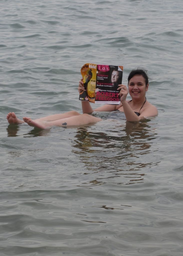 A woman smiles as she's floating in the Dead Sea in Jordan, posing for a picture with a magazine in her hands.