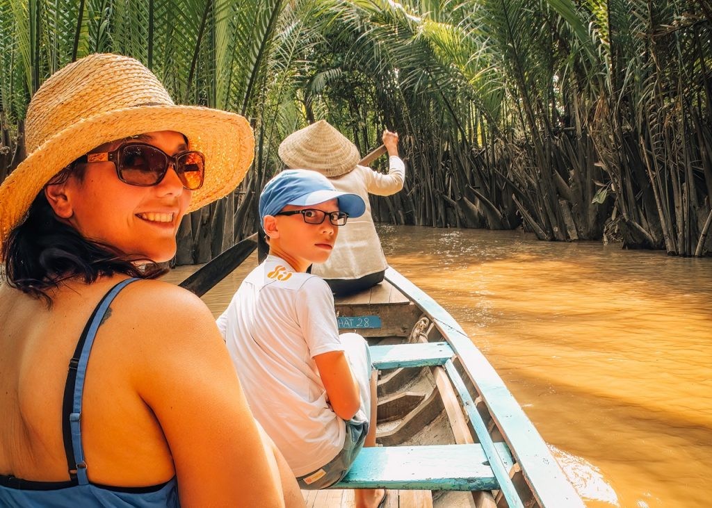 A mother and son are cruising the Mekong Delta in a row boat in Vietnam on a sunny day