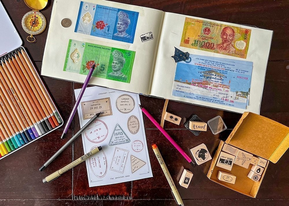 A scrapbook filled with Thai money and ticket stubs is accompanied by color pencils, stickers and stamps